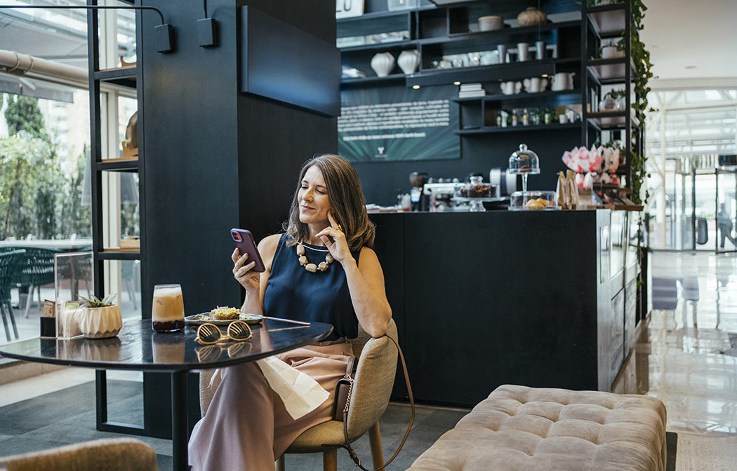 Elegante signora guarda lo smartphone in un caff&egrave;.